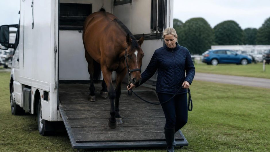 Horse owner leading a horse down the ramp of a motorised horsebox at a yard